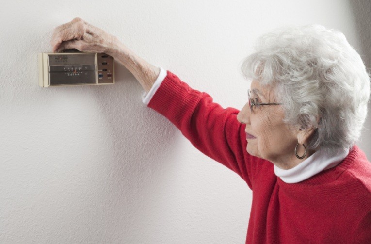 Elderly woman adjusting a wall thermostat
